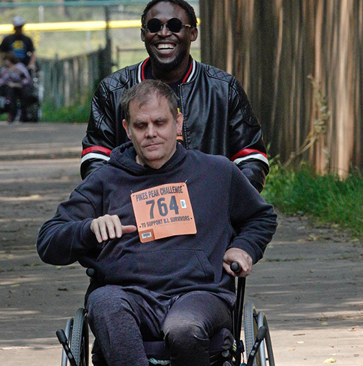 Man pushing another man in a wheelchair at the Manitou Walk.